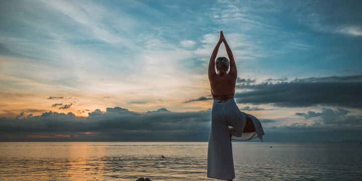 Strand bei Sonnenuntergang mit einer Frau welche eine Yogaübung macht