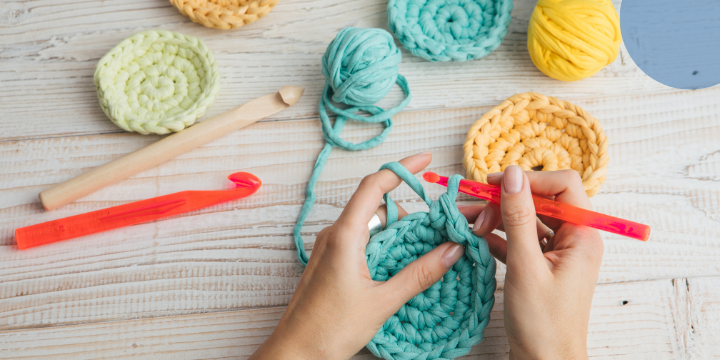 Eine Hand mit einer Häkelnadekl und viele bunte bereits gehäkelte Objekte